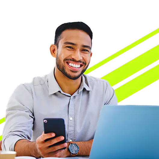 Homem alegre segurando celular em frente a um laptop.